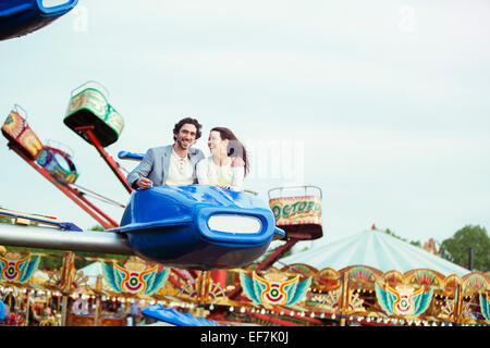 Couple enjoying ride sur carrousel en amusement park Banque D'Images