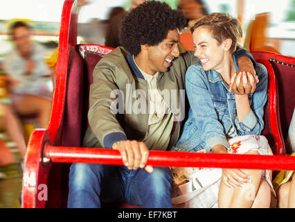 Cheerful couple sur carrousel en amusement park Banque D'Images