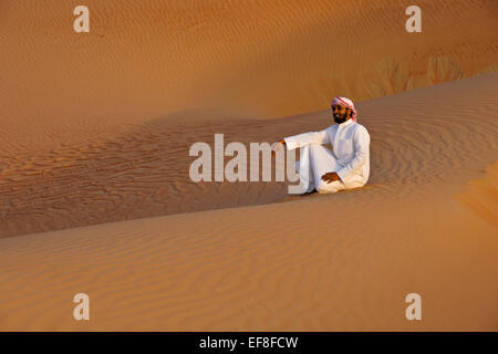 L'homme arabe en costume traditionnel assis dans les dunes de Liwa, Abu Dhabi, UAE Banque D'Images