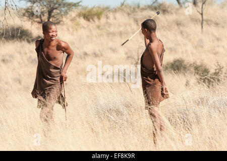 Deux jeunes portant des peaux de cuir Bushman partager un rire pendant une chasse dans les hautes herbes du Kalahari, la Namibie, l'Afrique Banque D'Images