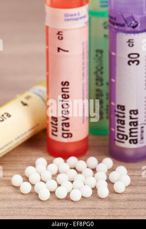 Globules homéopathiques éparpillés autour avec leurs conteneurs de couleur en forme de tube sur une table en bois Banque D'Images