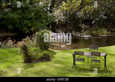 Une table et une chaise dans un jardin près d'un ruisseau Banque D'Images