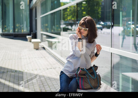 Woman sitting in street talking on mobile phone Banque D'Images