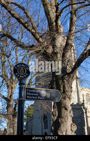 Panneau métallique pointant vers le château, le musée et la place du marché à Oakham, Rutland, avec le 14e siècle, l'église de Tous les Saints. Banque D'Images