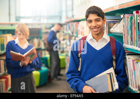 Portrait of teenage student standing with books in college library Banque D'Images