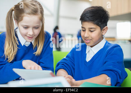 Garçon et fille portant des uniformes scolaires using digital tablet together Banque D'Images