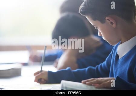 Collégiens écrit at desk in classroom Banque D'Images