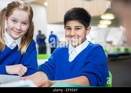 Portrait of smiling school enfants portant l'uniforme bleu sitting at desk Banque D'Images