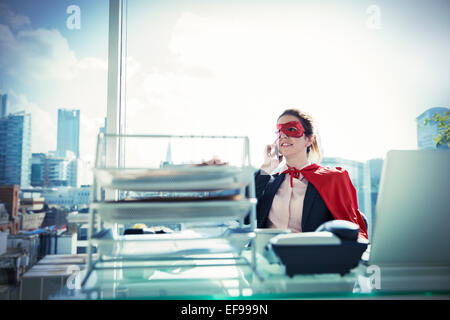 Businesswoman in Cape et masque parlant au téléphone au bureau 24 Banque D'Images