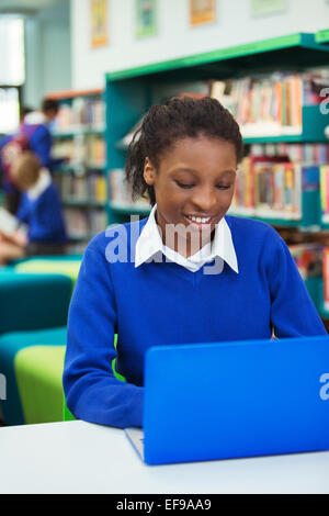 Smiling female student wearing blue school uniform using laptop in library