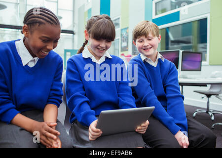 Les enfants de l'école primaire on the school uniforms holding digital tablet and smiling in classroom Banque D'Images