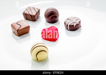 Chocolat en forme de coeur rouge avec praline sur une plaque blanche Banque D'Images