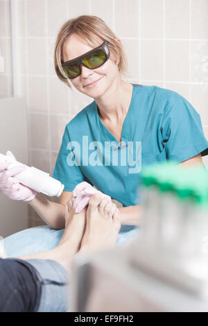 Smiling cosmetician travaillant avec le laser pour traiter les pieds Banque D'Images