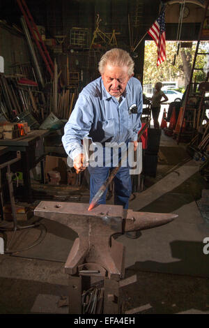 À l'aide d'un marteau, d'un forgeron à la vieille ville district de Tustin, CA, formes un barre de fer sur l'enclume de son atelier. Banque D'Images