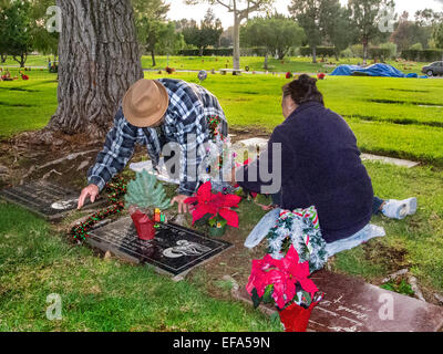 A Noël, un vieux couple décorer un membre de la pierre tombale dans un cimetière de l'Orange, CA. Banque D'Images