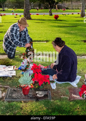 A Noël, un vieux couple décorer un membre de la pierre tombale dans un cimetière de l'Orange, CA. Banque D'Images