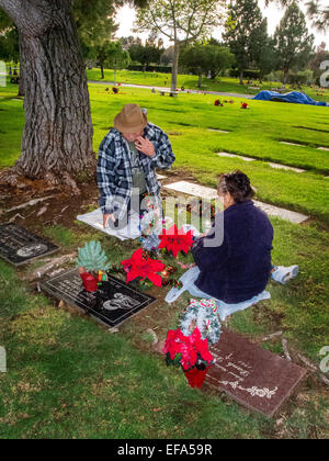 A Noël, un vieux couple décorer un membre de la pierre tombale dans un cimetière de l'Orange, CA. Banque D'Images