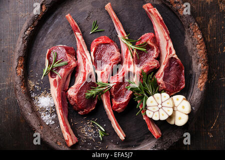 Côtes d'agneau frais de matières premières et d'herbes épicées sur fond sombre Banque D'Images