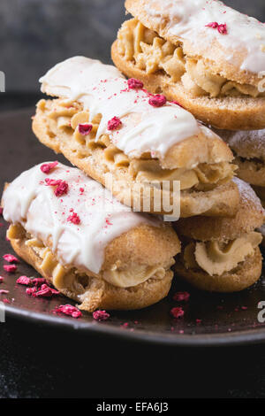 Plaque en céramique de mini éclairs au chocolat blanc, servi avec de la framboise sur fond sombre Banque D'Images