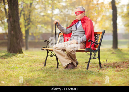 En tenue de super-héros principal triste assis dans un parc sur un banc en bois Banque D'Images