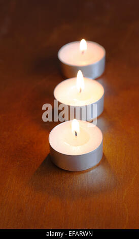 Trois blancs, allumé des bougies de thé en ligne sur une sombre, brunâtre, table en bois. Banque D'Images