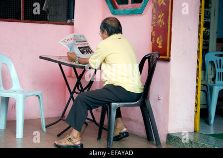 Un homme asiatique est en train de lire un journal de langue chinoise dans le centre de Phnom Penh, Cambodge. Banque D'Images