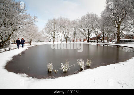 La neige a couvert Baddesley Ensor en Amérique du Warwickshire, Royaume-Uni. Deux personnes marchant autour de l'étang gelé Banque D'Images