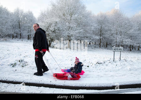 La neige a couvert Baddesley Ensor en Amérique du Warwickshire, Royaume-Uni. Un enfant est sledged à l'école le long de la Colline Les clés d'un adulte Banque D'Images