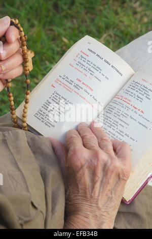 Une main de femme senior avec croix de bois sur un livre de prière franciscaine Banque D'Images