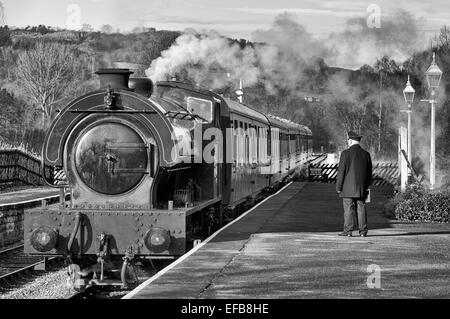 Le maître de la gare noir et blanc attendant la gare de Darley Dale alors qu'un train de voyageurs arrive typique des années 1940, 1950 et 1960 Banque D'Images