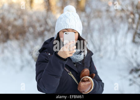 Belle jeune femme asiatique en hiver paysage prend photo de l'afficheur avec un smartphone. Banque D'Images