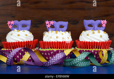 Mardi Gras cupcakes avec masque violet toppers sur bleu foncé de style rustique en bois vintage table. Banque D'Images