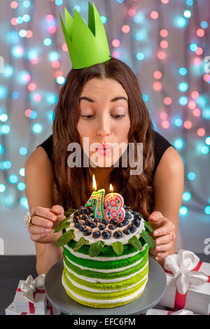 Dix-huit fille avec happy birthday cake faire exploser des bougies sur fond clair de fête Banque D'Images