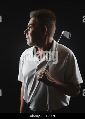 Homme mature golfer portant une chemise blanche et il est titulaire d'un club de golf de fer sur son épaule et il à l'écart - studio shot, noir b Banque D'Images