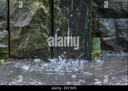 L'eau de pluie d'une fuite du tuyau d'évacuation endommagé coulent sur un trottoir. Banque D'Images