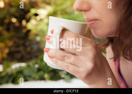 Femme souriante détient white tasse de café dans ses mains. Photo extérieure de style vintage gros plan Banque D'Images