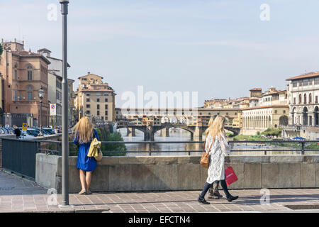 Fille en robe bleue avec de longs cheveux blonds se situe à rail de Ponte alle Grazie contemplant Arno comme 2 autres jolies filles passent par Banque D'Images