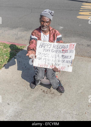 Un mendiant est assis sur un trottoir et est titulaire d'un signe avec sa main pour demander de l'argent à Santa Barbara, en Californie. Banque D'Images