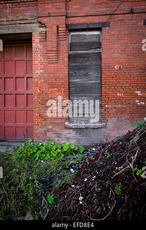 Un vieux bâtiment en brique rouge, abandonné avec une porte et des fenêtres. Banque D'Images