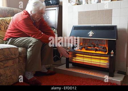 Ancien pensionné en essayant de garder au chaud à côté d'un radiateur électrique Banque D'Images