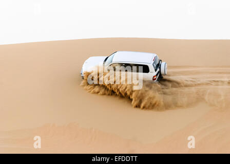 Un 4x4 hors route jeep lance de sable comme il se conduit sur le côté d'une dune de sable dans le désert de la péninsule arabique Banque D'Images