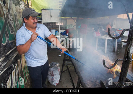 Oaxaca, Mexique - Un homme cuisiniers viande à un incendie dans un restaurant en plein air. Banque D'Images