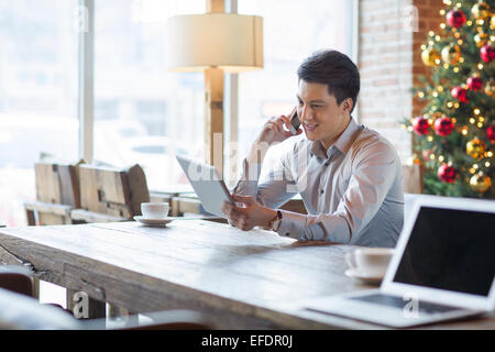 Young man talking on phone and using digital tablet in cafe Banque D'Images