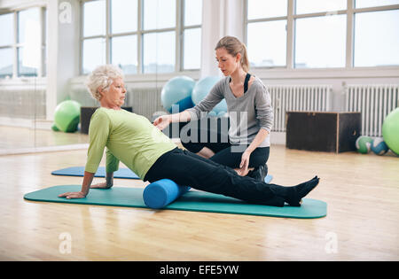 Physiothérapeute travaillant avec active senior woman at rehab. Vieille Femme exerçant à l'aide de rouleau en mousse avec un entraîneur personnel. Banque D'Images