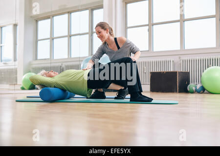 Formateur senior woman femme demandant va exercer sur un rouleau en mousse. Femme aîné faire pilates workout avec instructions personnelles Banque D'Images