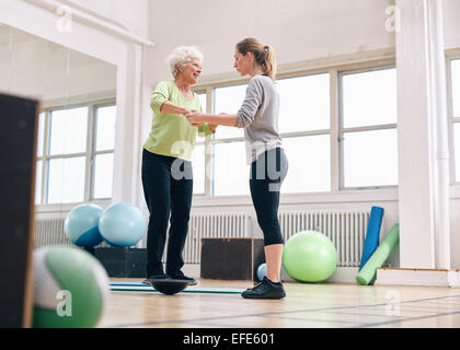 Femme trainer helping senior woman in a gym entraînement avec le bosu balance plate-forme de formation. La femme d'être assisté d'une salle de sport Banque D'Images