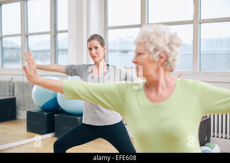 Deux femmes de faire des étirements et de l'aérobic de l'exercice dans la salle de sport. Female trainer en arrière-plan avec des hauts femme en face pendant l'activité physique Banque D'Images
