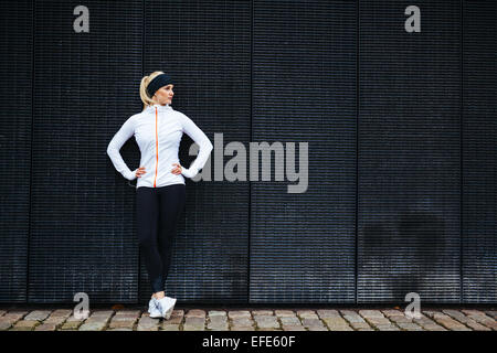 Femme déterminée se reposant après le jogging dans la ville. Toute la longueur de balle sporty young woman relaxing après exécution de l'exercice. Banque D'Images