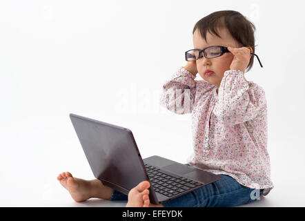 Petite fille avec des lunettes à regarder sur l'ordinateur portable Banque D'Images