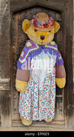 De taille gigantesque ours portant robe floral coloré, chapeau de paille et châle de laine avec des fleurs, contre l'ancienne porte de bois de shop Banque D'Images